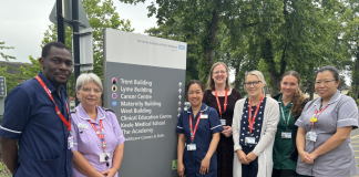 7 Members of the clinical research team standing next to a totem style sign showing directions to many of the hospital departments