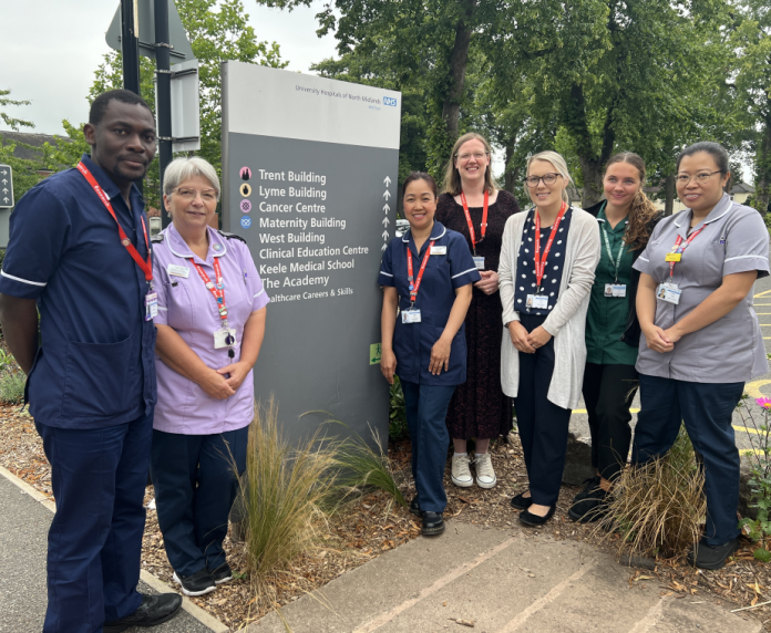 7 Members of the clinical research team standing next to a totem style sign showing directions to many of the hospital departments
